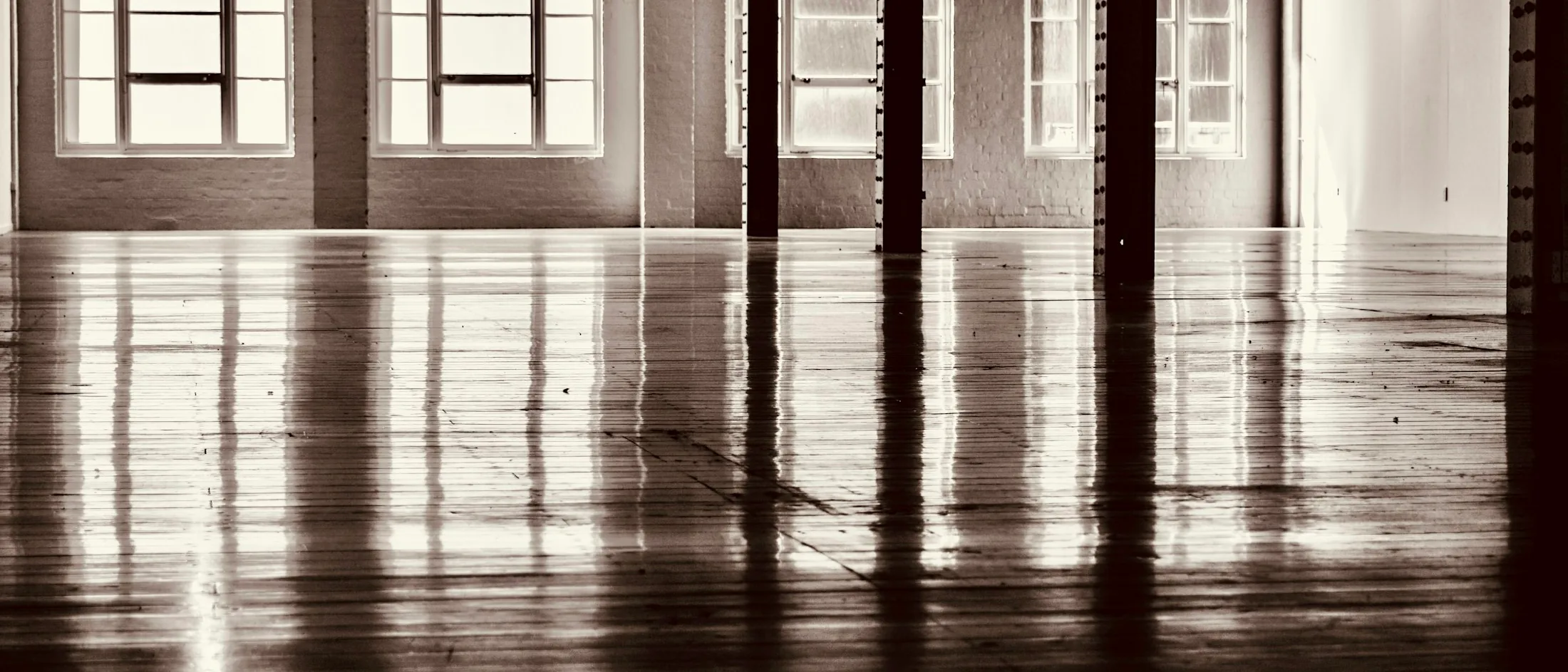 Leere Fabriketage mit Holzboden, Stützen und Fensterreihen, lichtdurchflutet