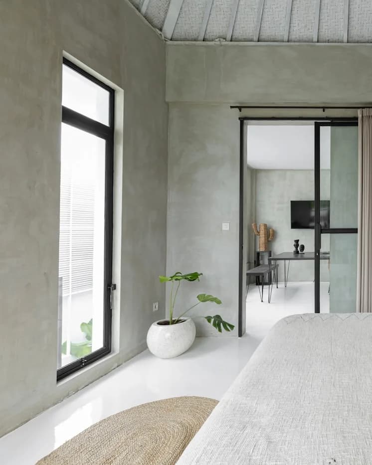 Möbliertes Zimmer mit Bett, Betonwand und viel Tageslicht